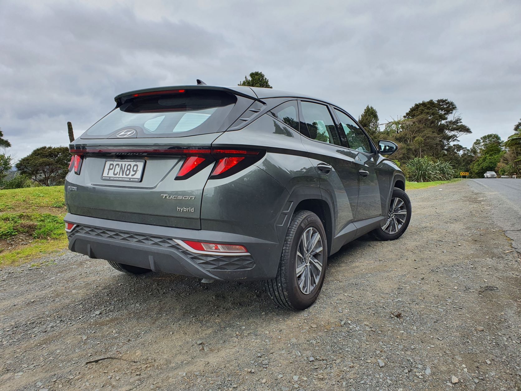 Rear three quarters view of the 2022 Hyundai Tucson Hybrid in green with a backdrop of nature