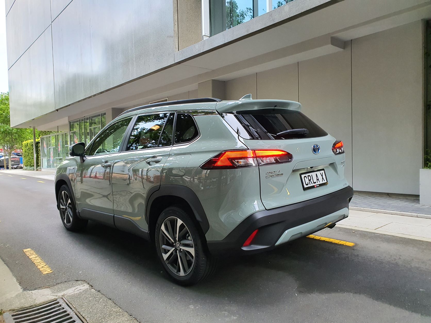 Rear three quarters view of a 2022 Toyota Corolla Cross Limited Hybrid E-Four AWD with a building in the background