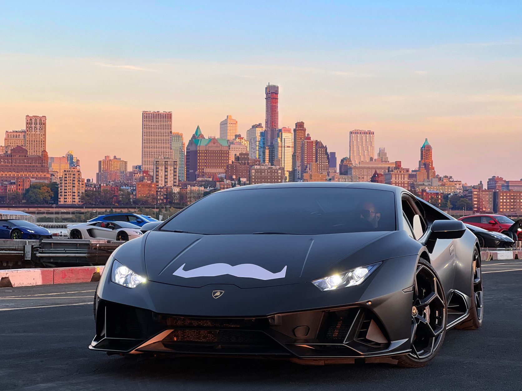Moustache logo stickered on the nose of a matte black Lamborghini Huracan EVO on a Movember "Bull Run"