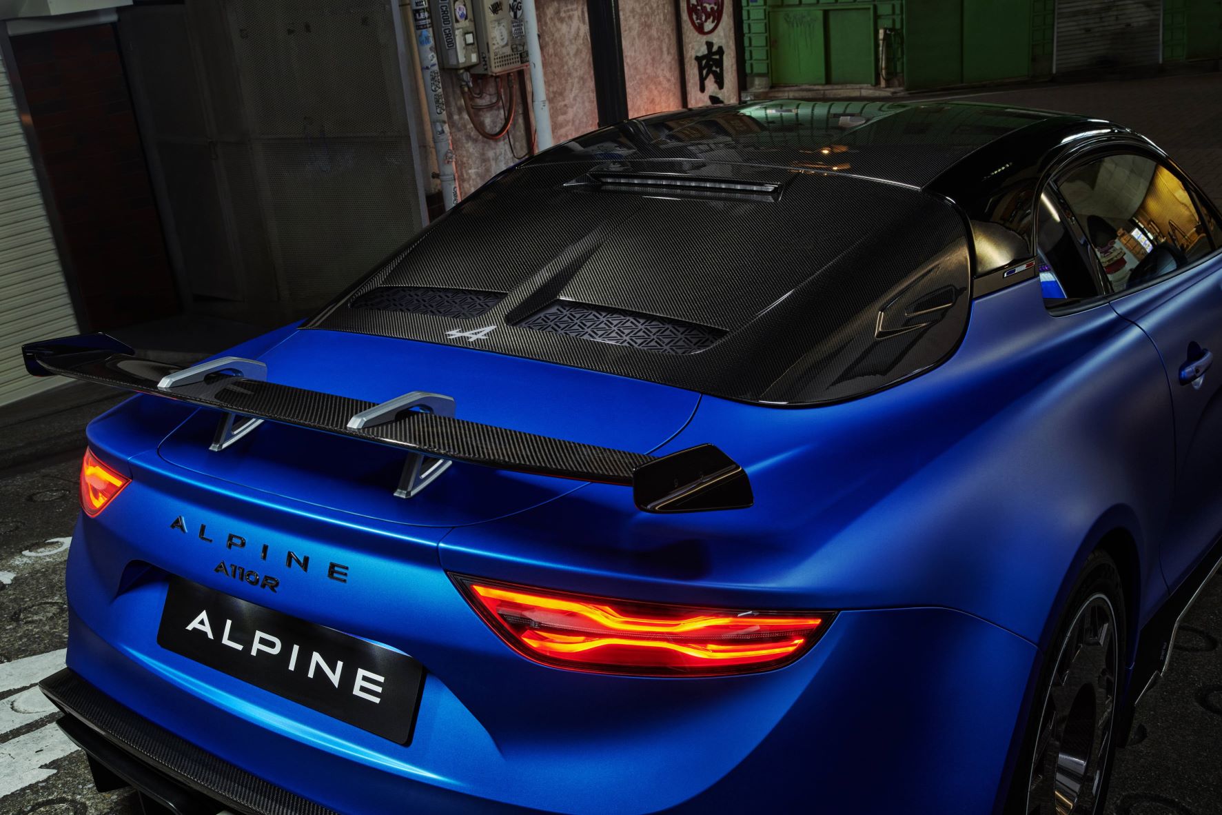 Close-up photo of the rear of a blue Alpine A110R, highlighting the carbon fibre spoiler and rear window.
