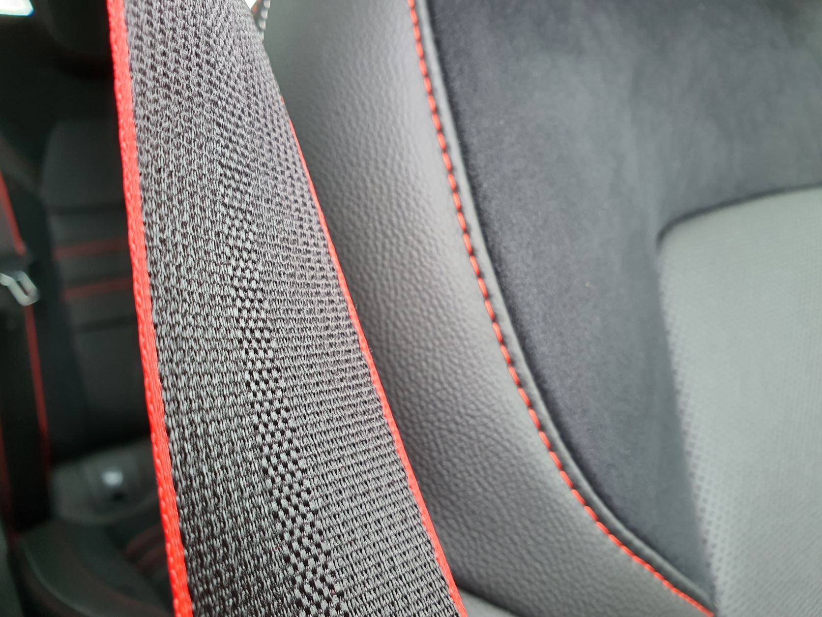 Photo of the seatbelt in a Renault Arkana R.S Line with red stitching highlights with the black leather seats in the background.