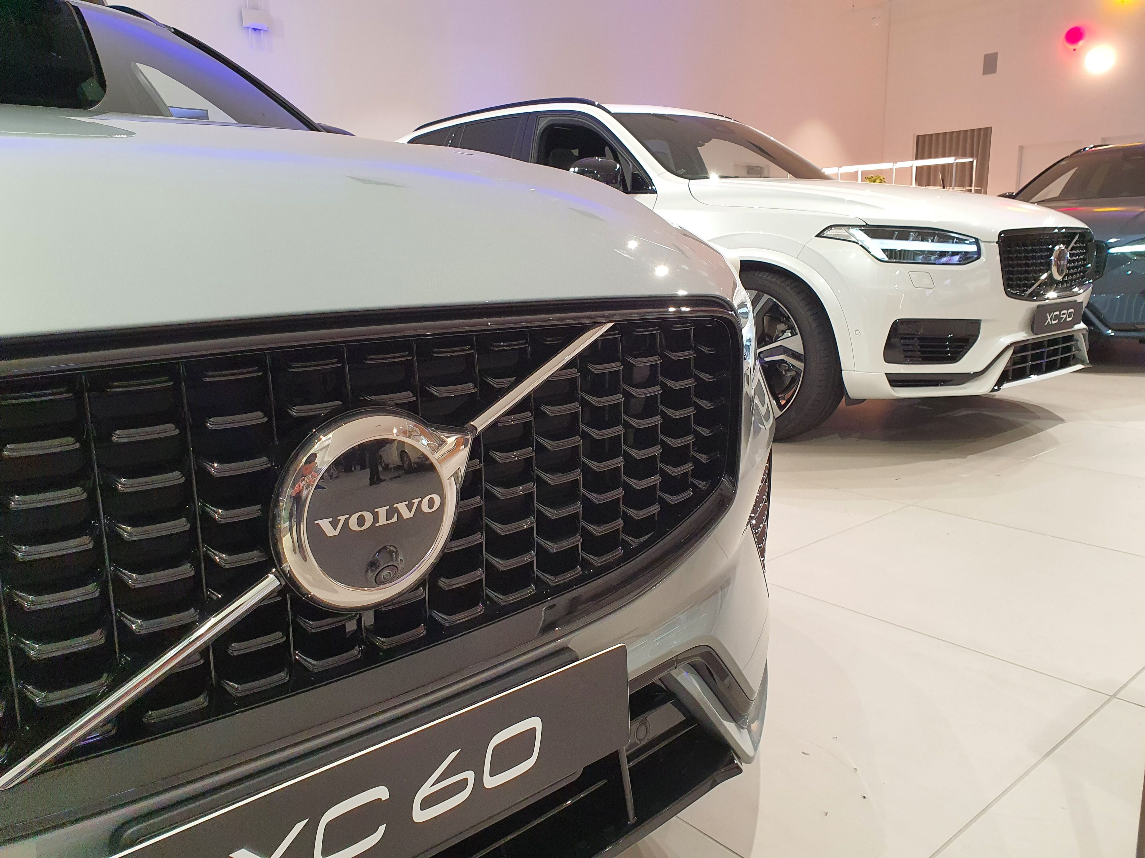Close up shot of the Volvo badge on the front of an XC60 with a Volvo XC90 in the background
