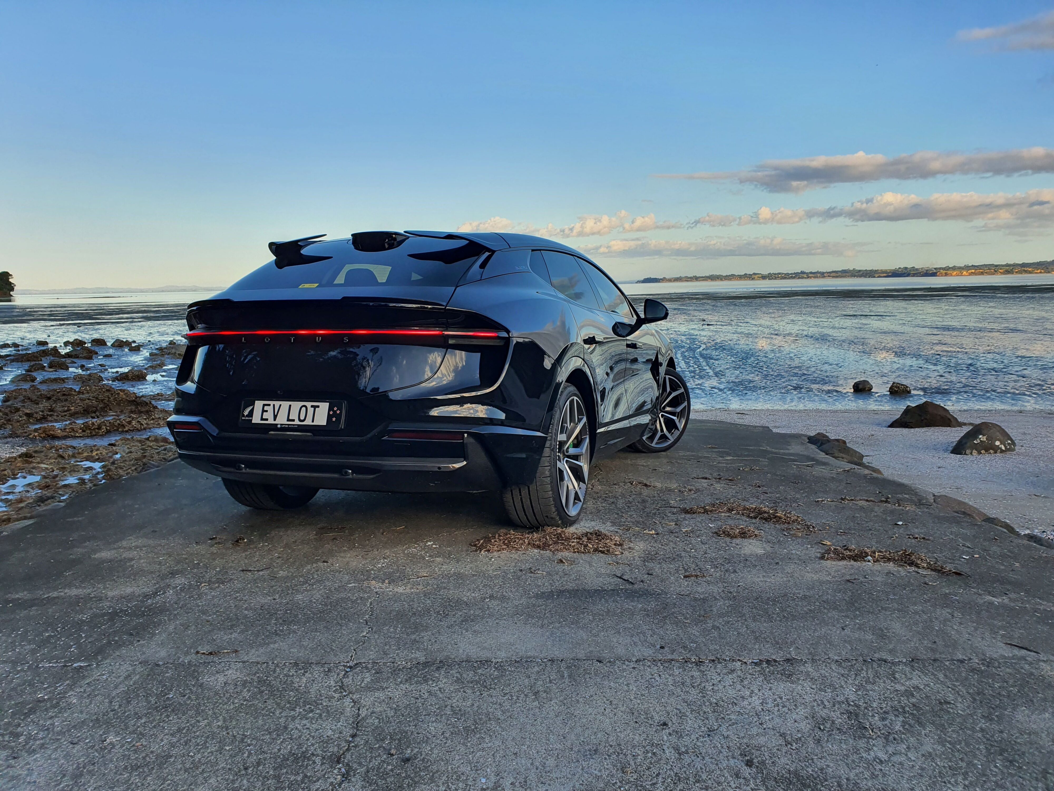 Rear three quarters view of a 2024 Lotus Eletre S in Black with a coastal background.