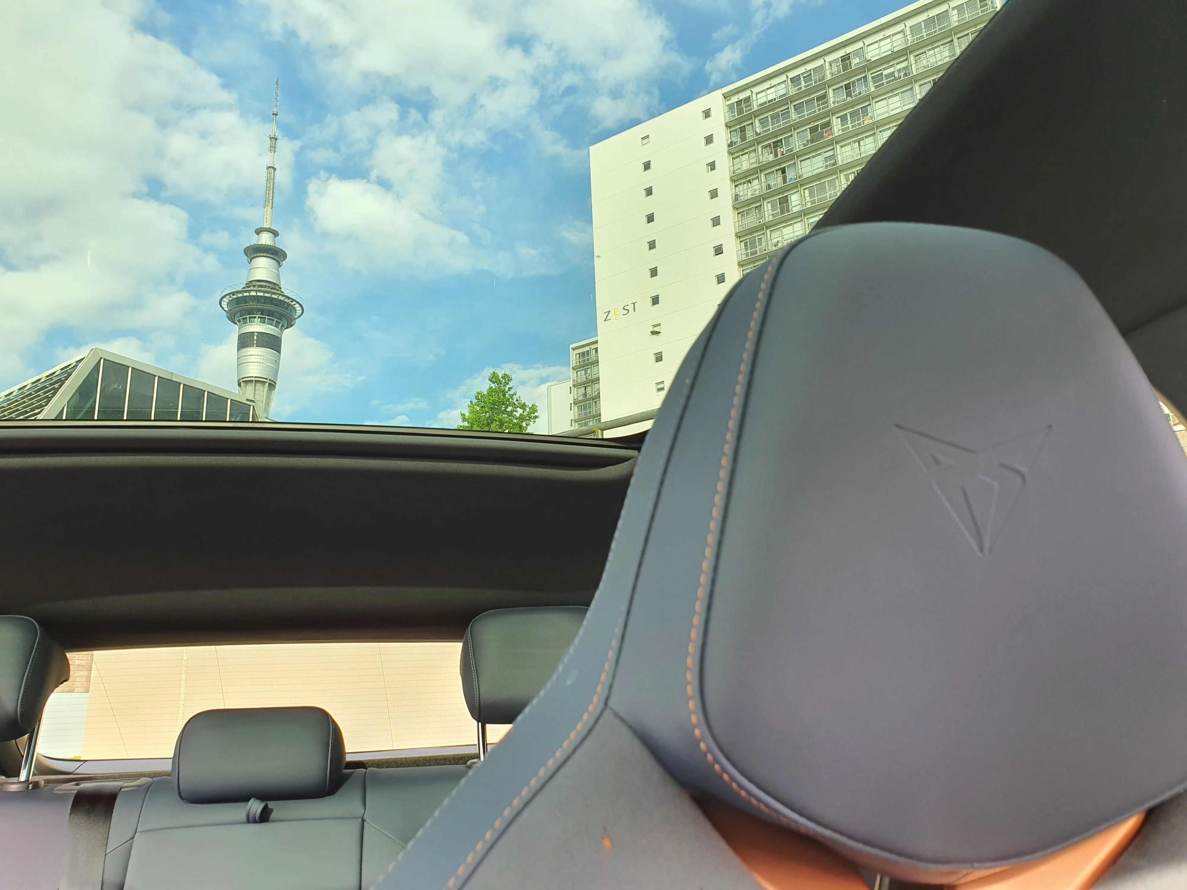 View through the glass roof of a 2025 Cupra Tavascan VZ in Tavascan Blue with the Auckland Sky Tower in the background.