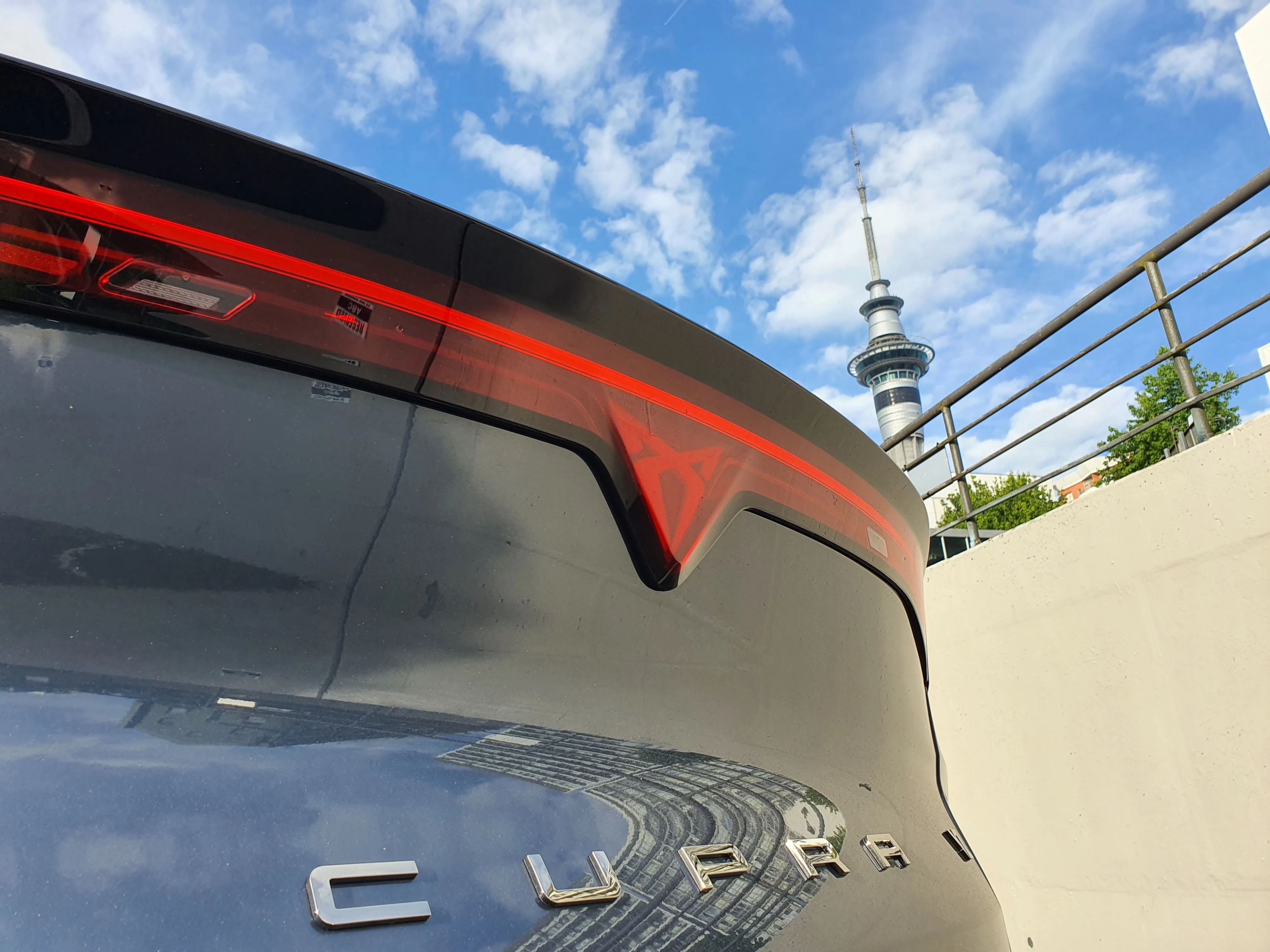 Rear view of a 2025 Cupra Tavascan VZ in Tavascan Blue with the Auckland Sky Tower in the background.