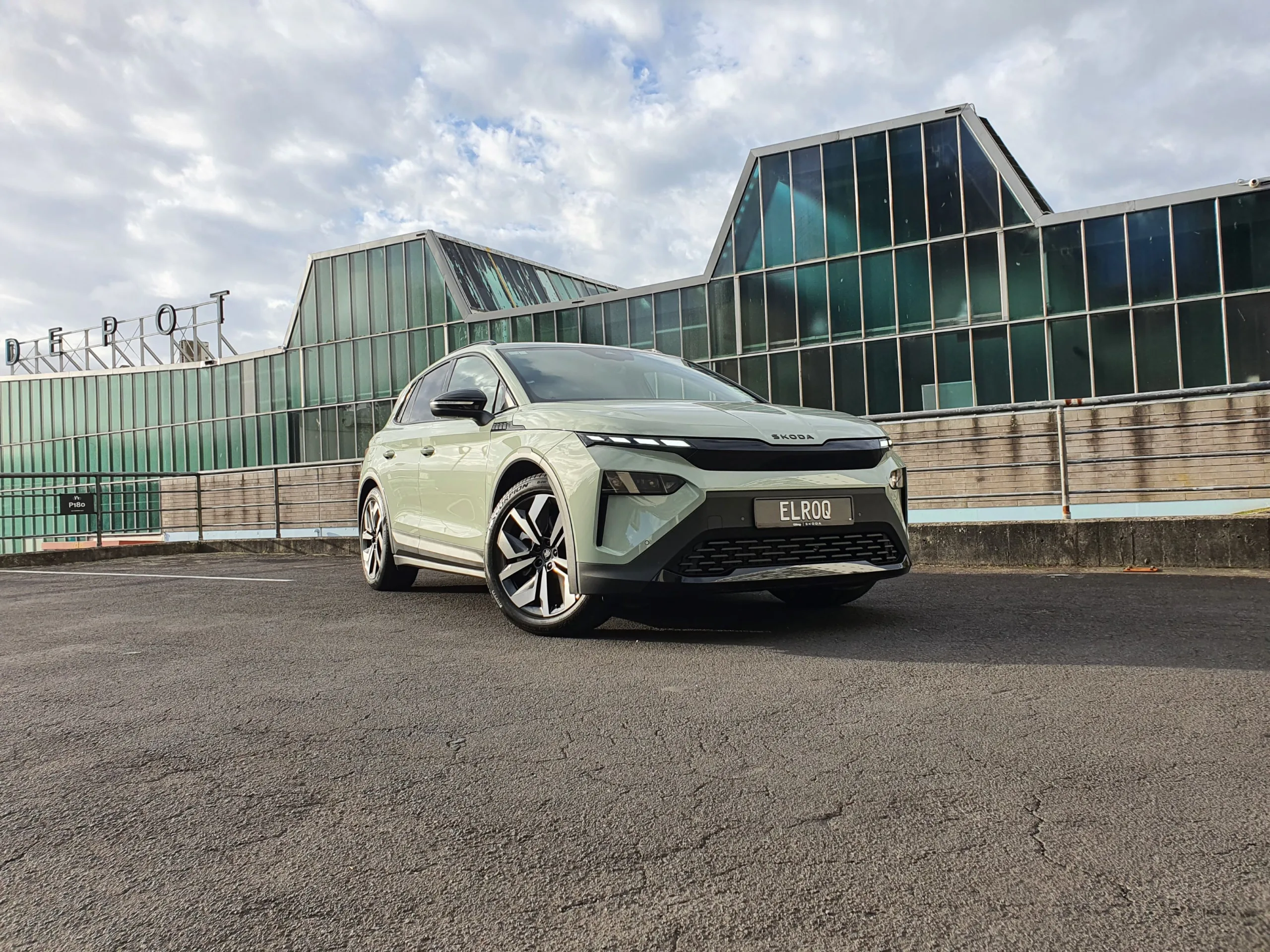 Front three quarters view of a 2026 Skoda Elroq Sportline in Timiano Green in front of an industrial building.