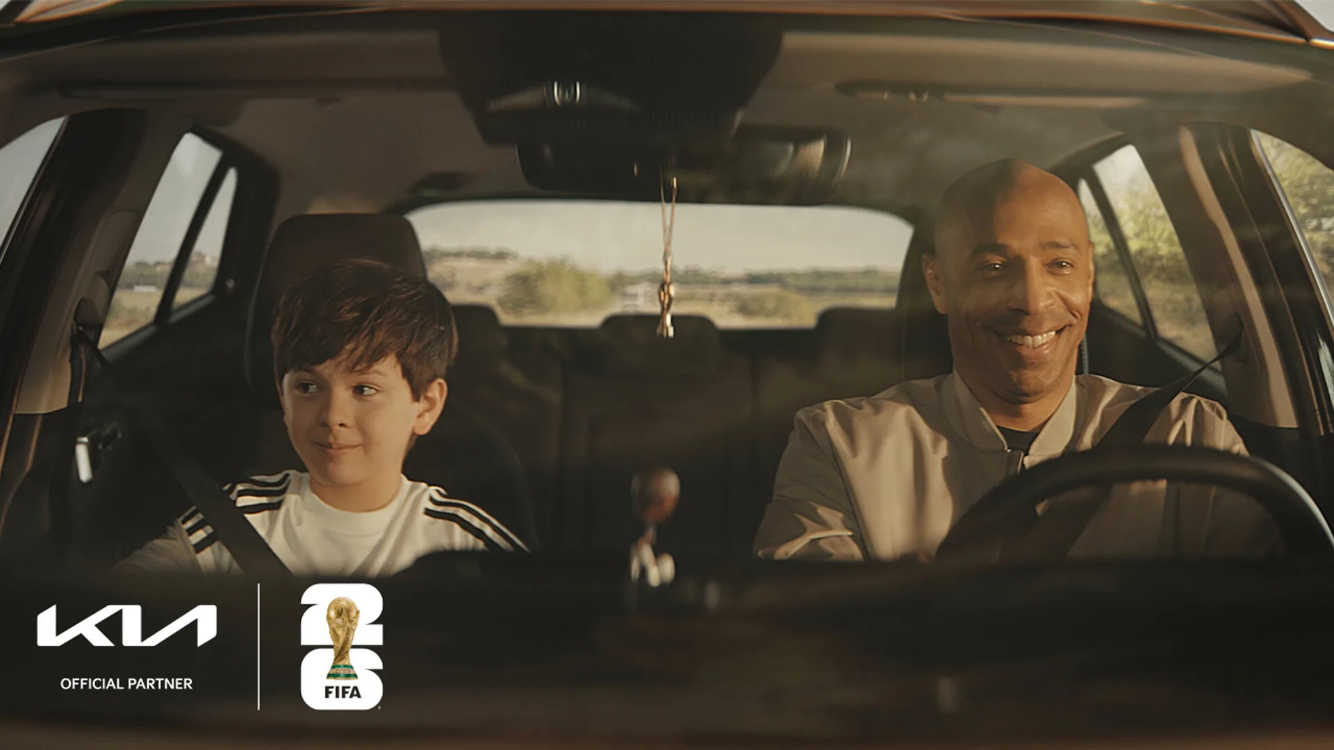 Photo of Thierry Henry and an actor inside a Kia car, promotional photo for the FIFA World Cup 2026.
