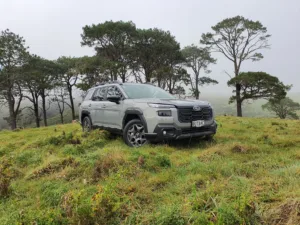 Front three quarters view of a 2026 Subaru Outback AWD in River Rock Pearl with a forest in the background.
