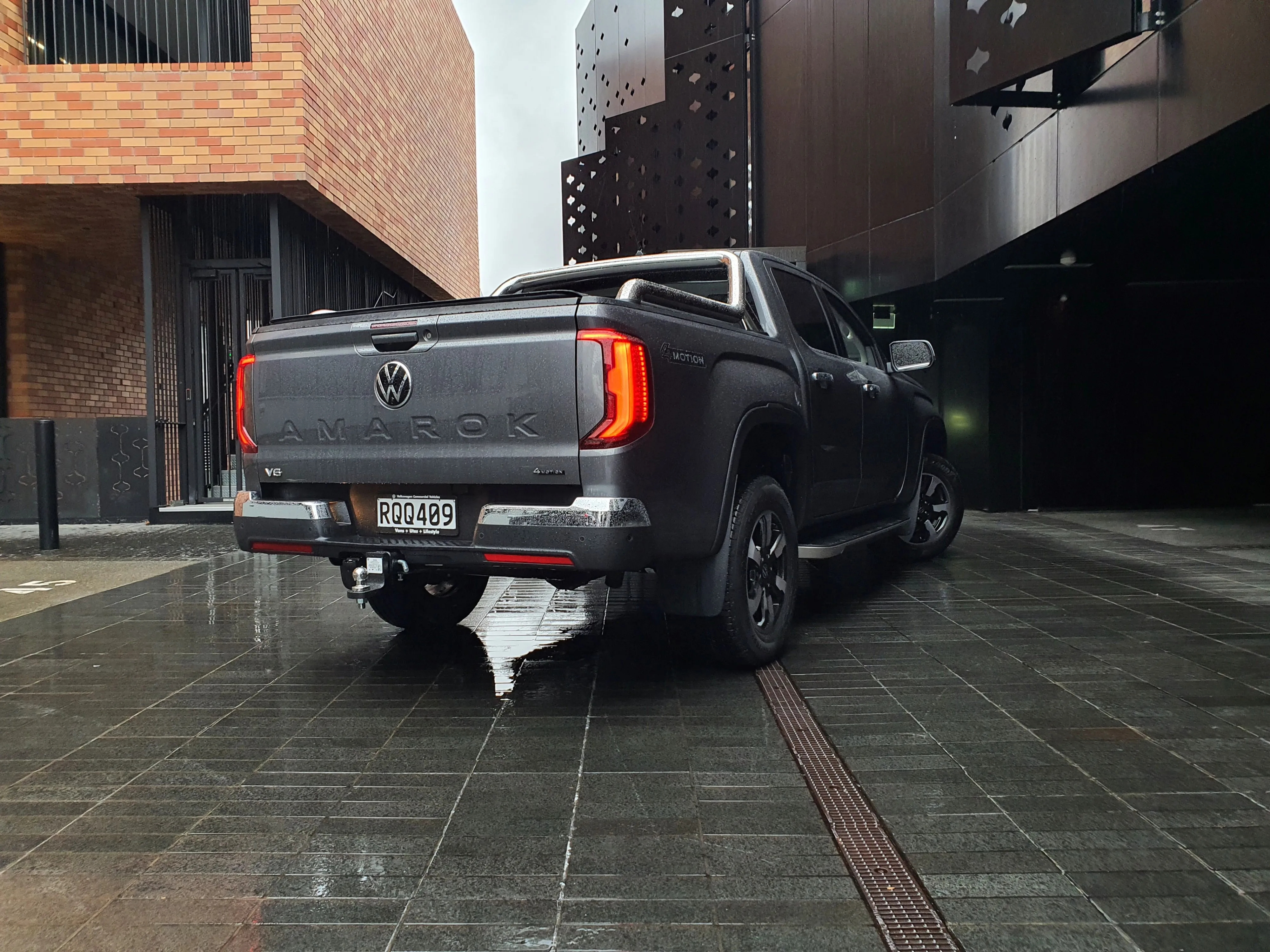 Rear three quarters view of a 2026 Volkswagen Amarok V6 Style in Carbonite Grey with an urban background.