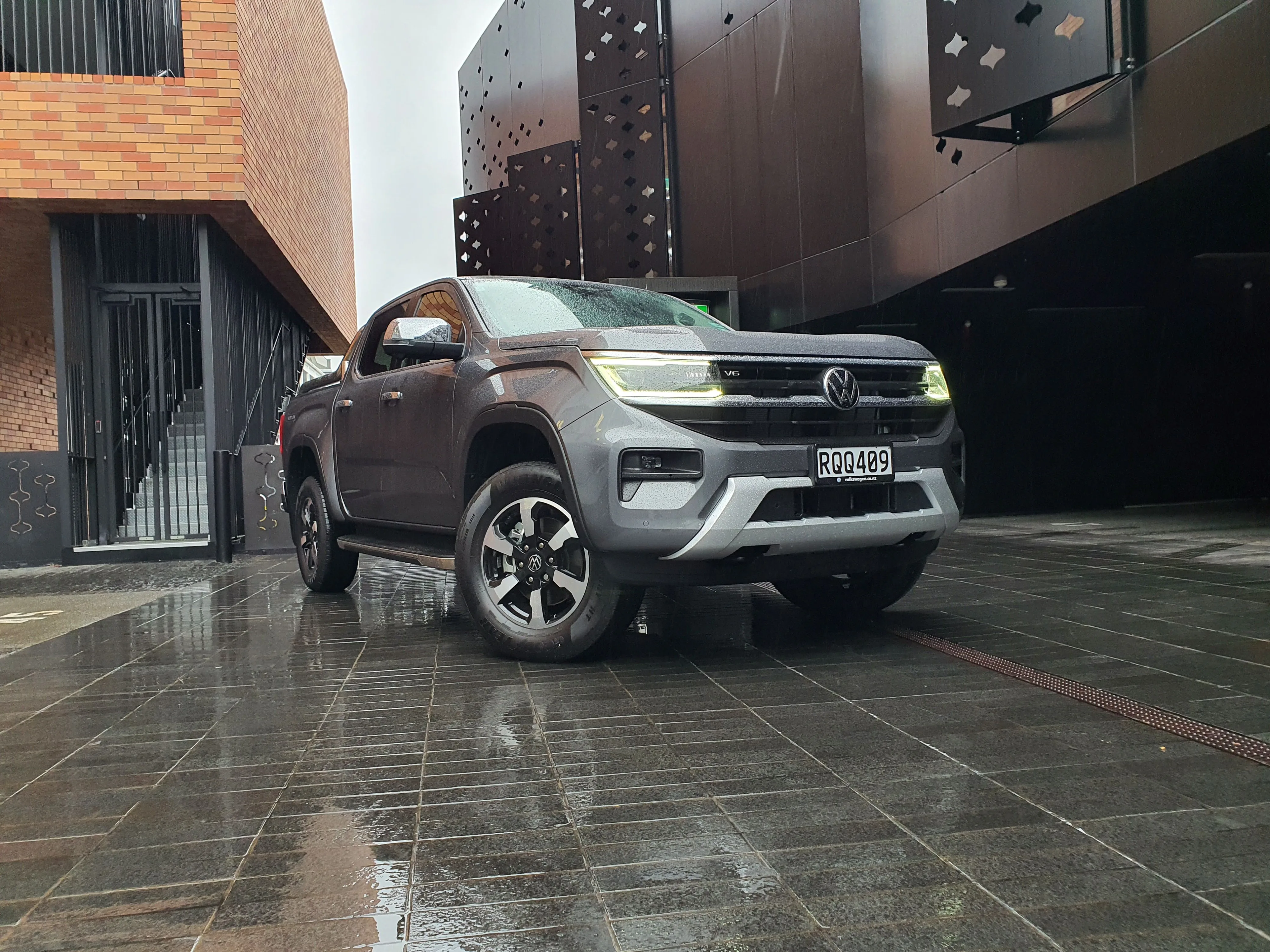 Close up front three quarters view of a 2026 Volkswagen Amarok V6 Style in Carbonite Grey with an urban background.