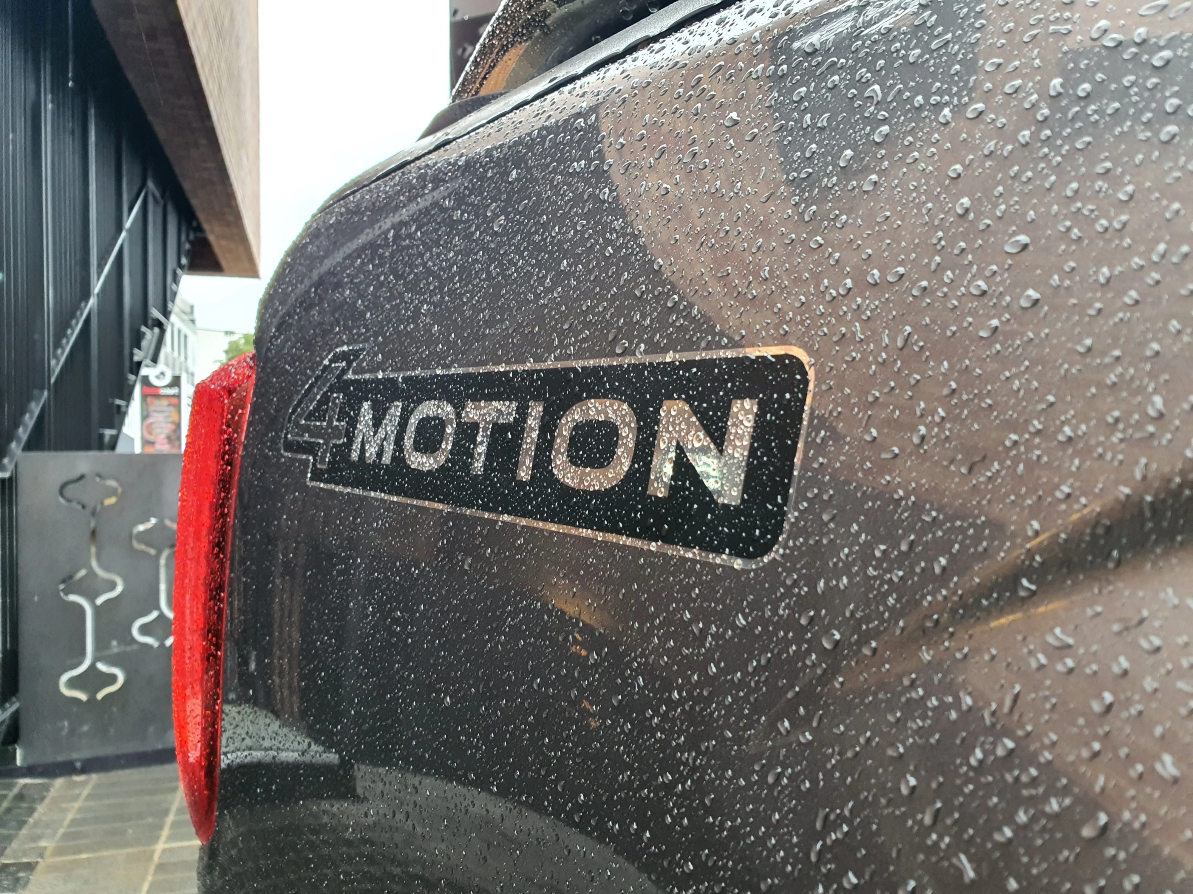 Close up of the 4Motion badge on the rear right of a 2026 Volkswagen Amarok V6 Style in Carbonite Grey with an urban background.